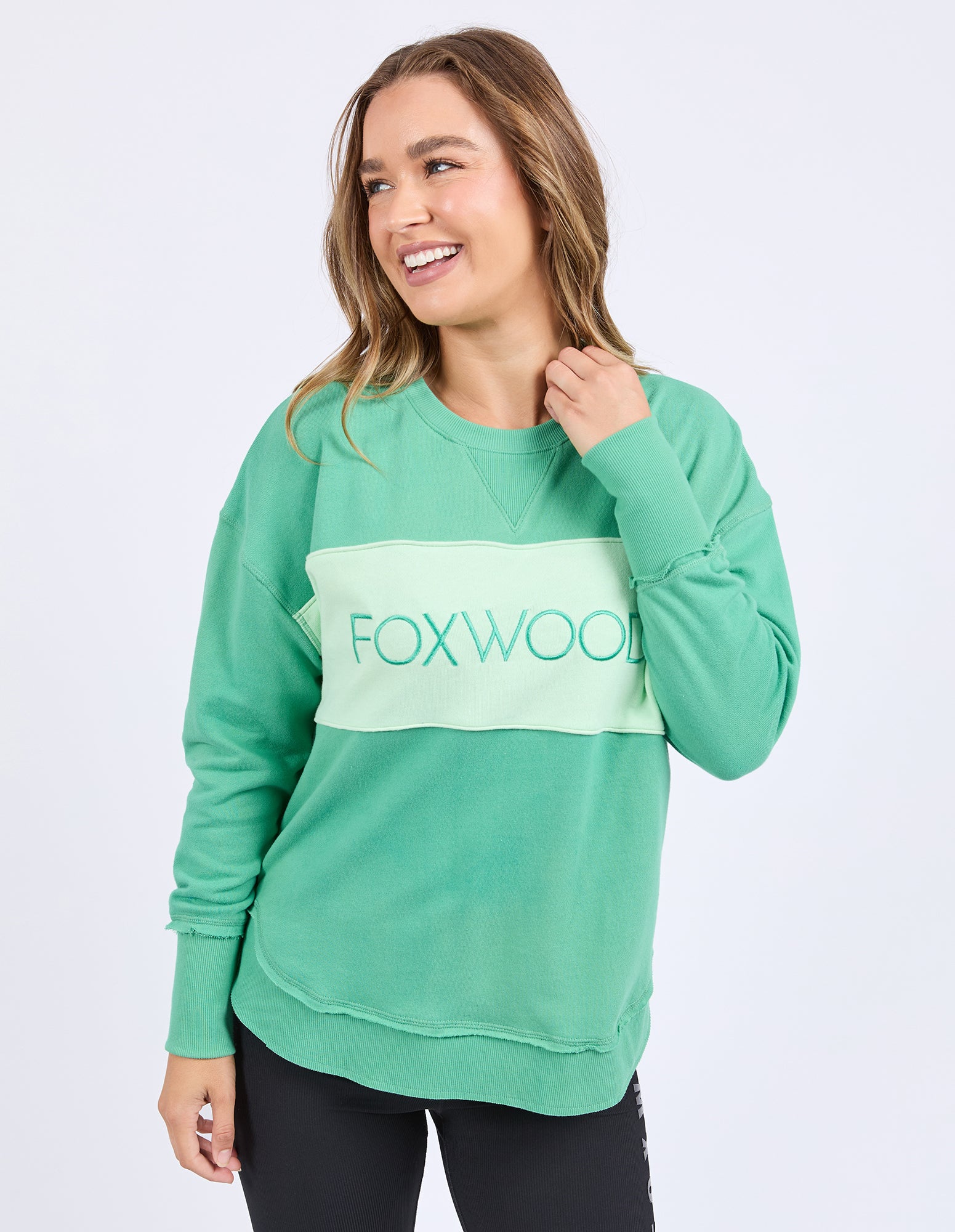 Woman wearing a green cotton tonal crew sweatshirt with 'FOXWOOD' logo on front.