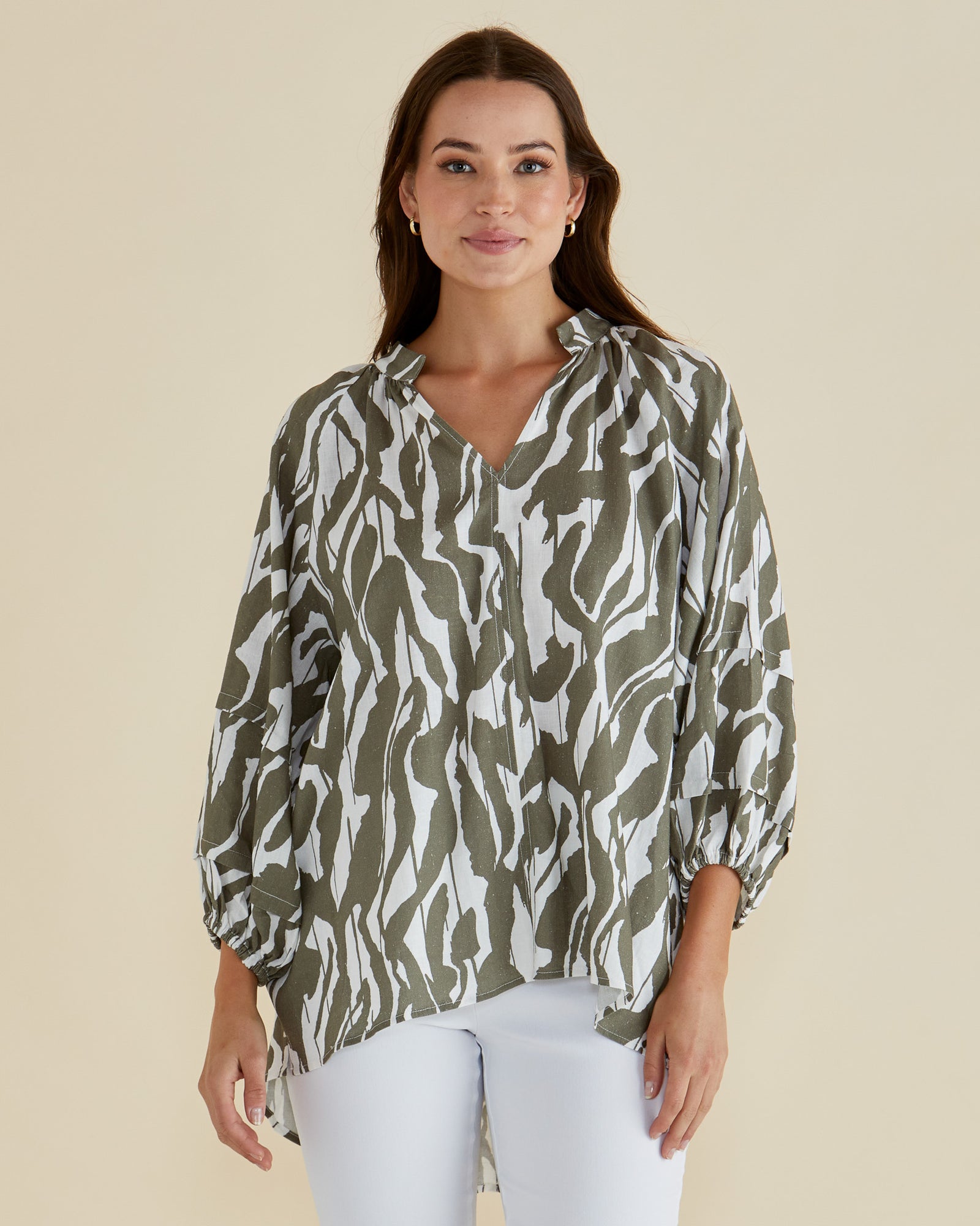 Woman wearing the Grazia green and white patterned blouse with long sleeves, a vneck and high low hem by Betty Basics.