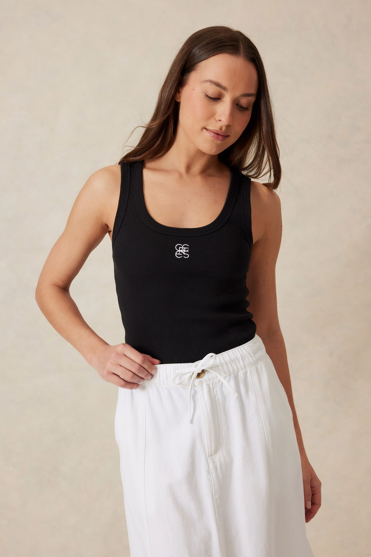 Woman wearing a sleeveless black scoop neck tank top with monogrammed ceres life on the front in white.