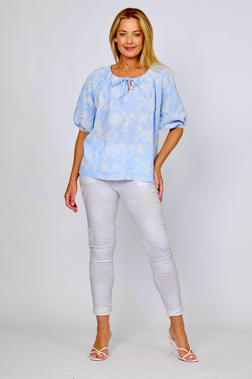 Woman wearing broderie top with embroidered flowers in white, short sleeves and a pull tie gathered neck by La Strada.