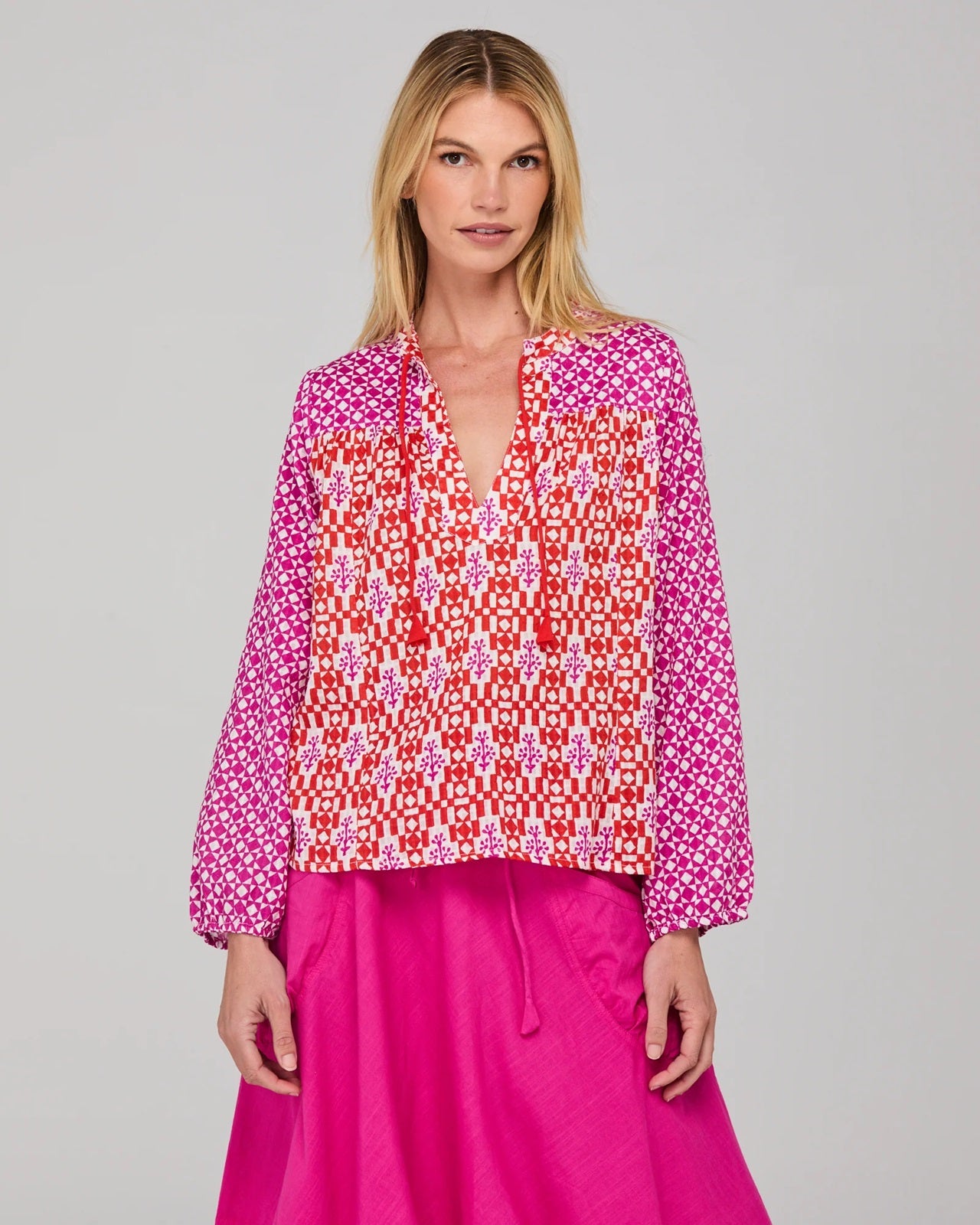 Model wearing a patterned cotton Fleetwood Top in Spliced Naples a pink, white and red print with long sleeves a v-neck and straight hem.