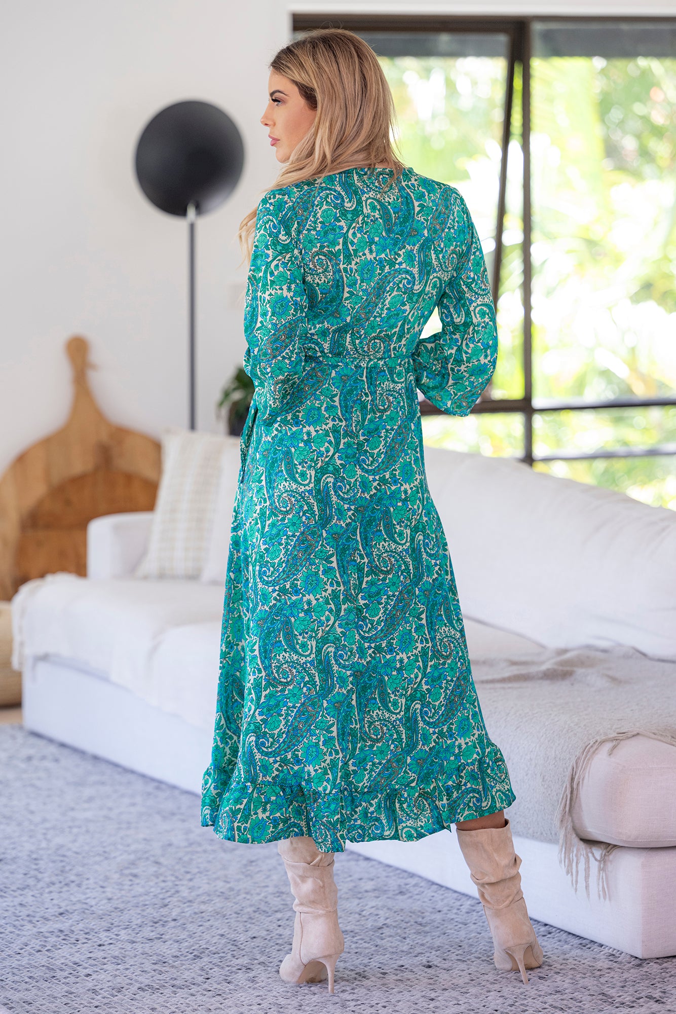 lady wearing Cienna's Beatrix silk blend boho wrap midi dress in green, blue and white paisley print with long sleeves and a ruffle hem. 