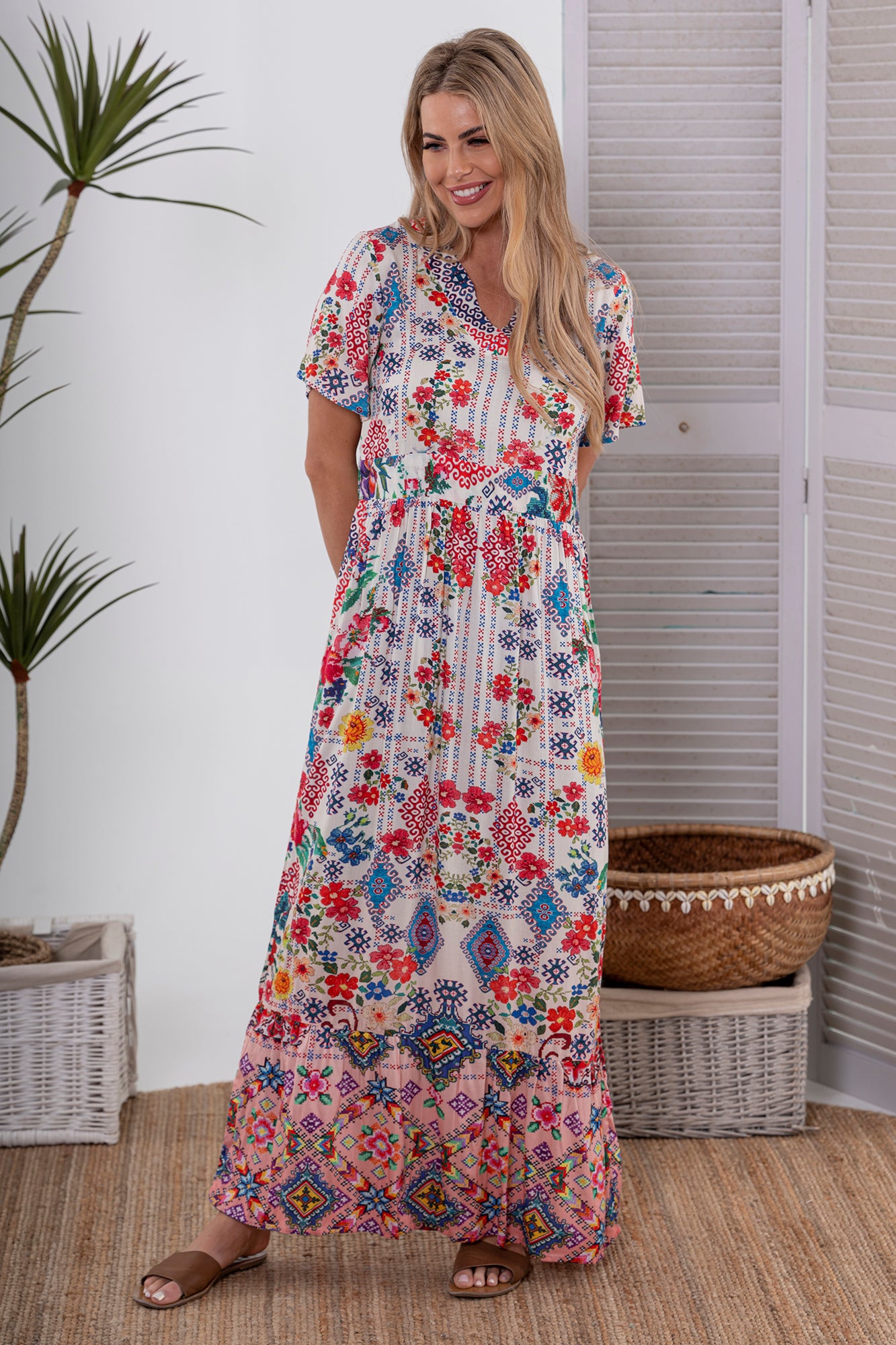 Woman wearing Cienna's cross stitch print maxi dress in white, blue red and pink with short sleeves and a v-neck.