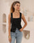 Woman wearing a square neck, black sleeveless tank top with wide straps and a split at the front.