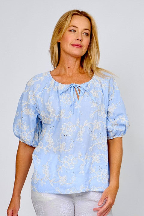 Woman wearing broderie top with embroidered flowers in white, short sleeves and a pull tie gathered neck by La Strada.