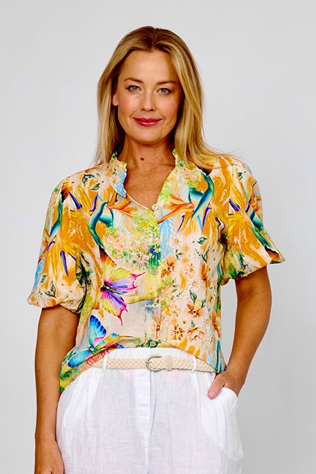Woman wearing the tropical frill collar shirt by La Strada with short leeves, vneck in orange, blue, green and beige with flowers, birds of paradise and butterflies.