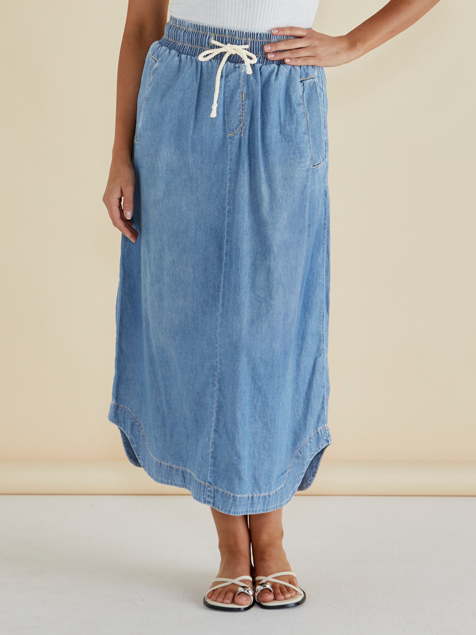 Woman wearing Betty Basic's Brunch Denim Skirt with a tie waist, pockets and a features curved side splits.