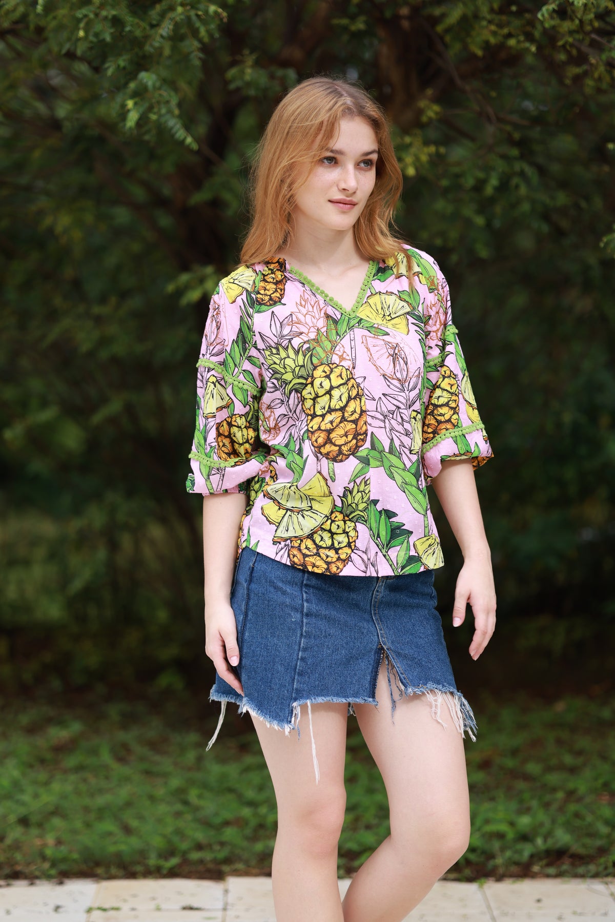 Ladies blouse with pineapple print in pink, yellow and green with pom poms on the neck.