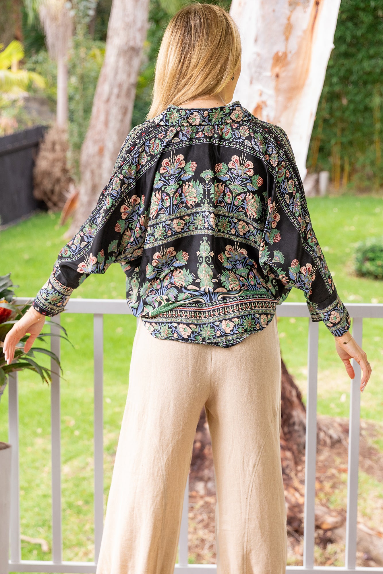 Woman wearing the Myra Silk Blend Long Sleeve Boho Blouse from Cienna in black, green and blue floral print.