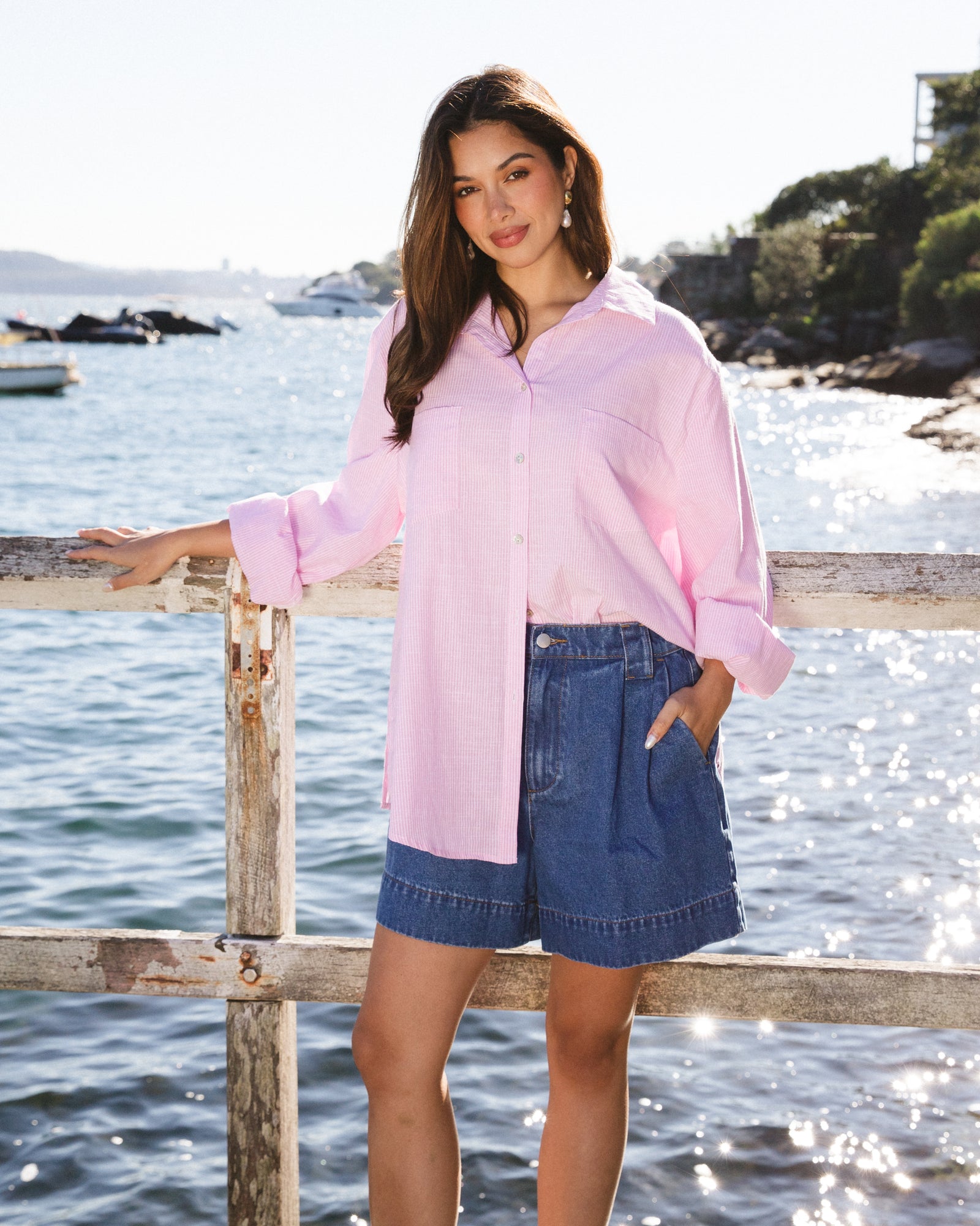 Woman wearing Marina striped shirt in pink and white thin stripes with collar and button up front with long sleeves with cuff by Label of Love.