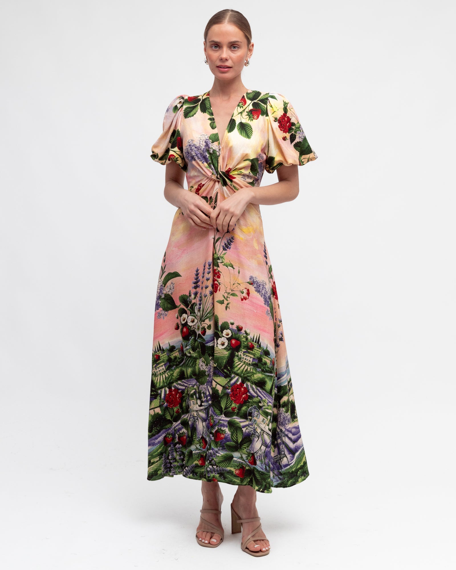 Model wearing the twist dress with strawberries and bulding print on a pink sunset background by white closet.