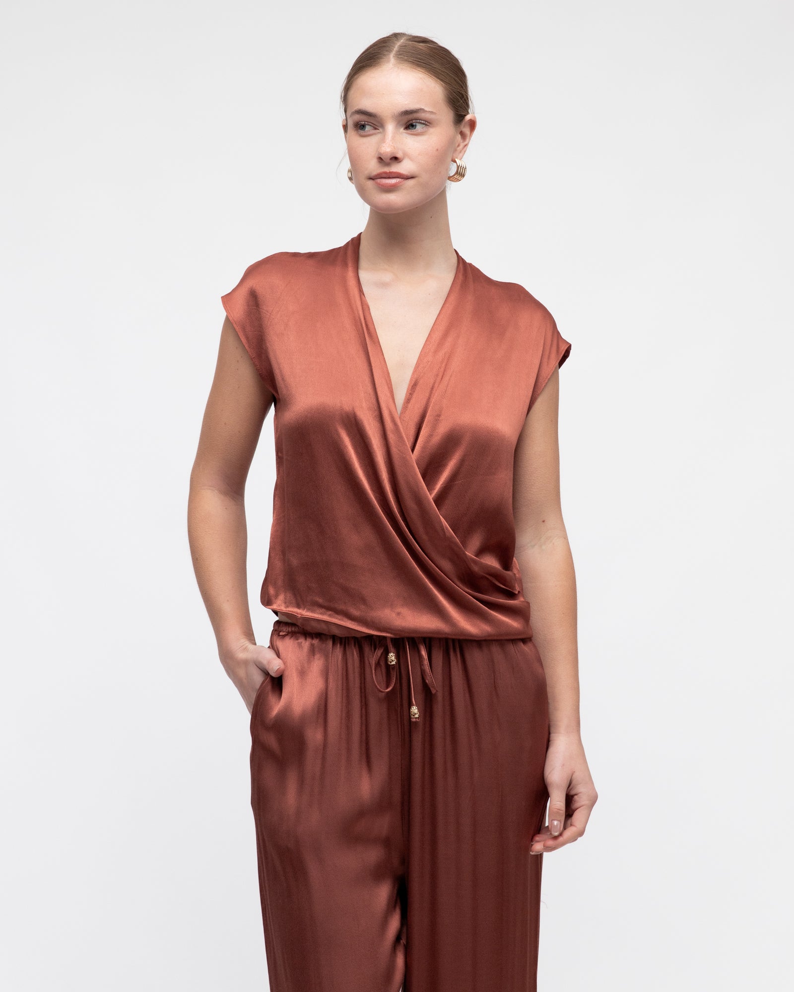 Woman wearing White Closet's Hera Cross Over Satin Top in Rose Pink with a deep v-neck, short cap sleeves and a soft silky feel.