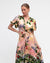 woman wearing pink floral and building print twist front dress from white closet.