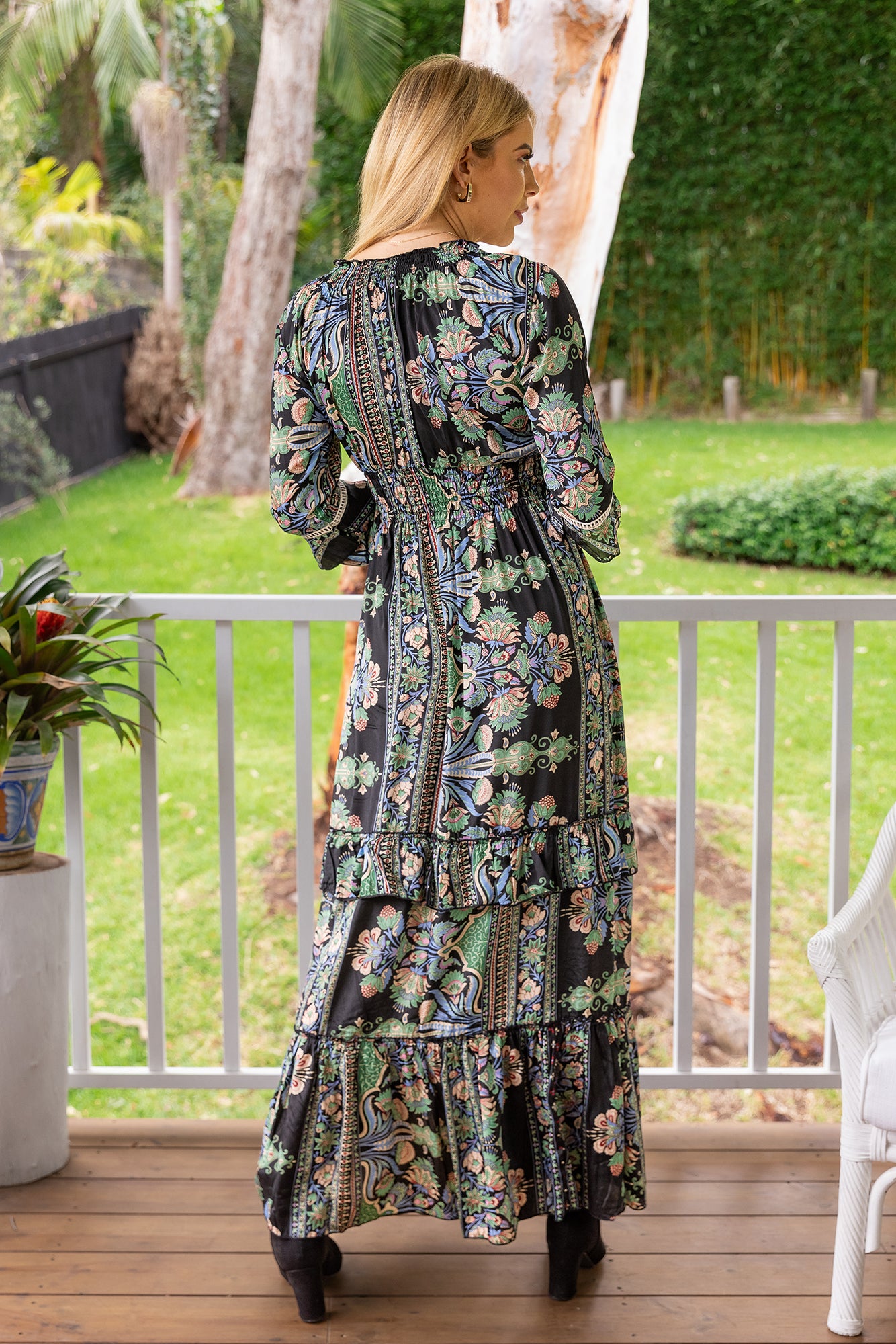 Lady wearing Cienna's Silk blend Myra Bohemian maxi dress with a v-neck, shirred under bust, long sleeves and a tiered skirt with ruffles in a goregous black, green, blue and honey toned floral paisley print.