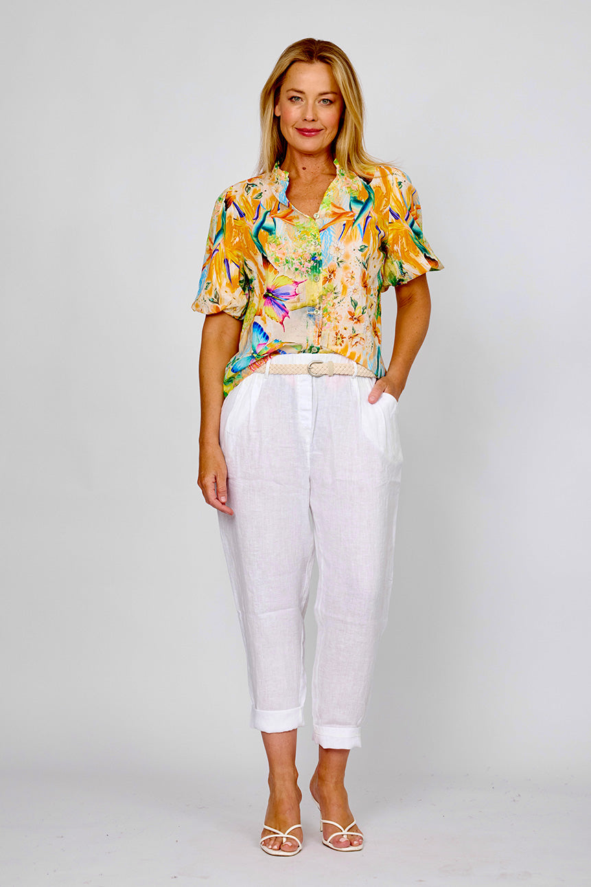 Woman wearing the tropical frill collar shirt by La Strada with short leeves, vneck in orange, blue, green and beige with flowers, birds of paradise and butterflies.