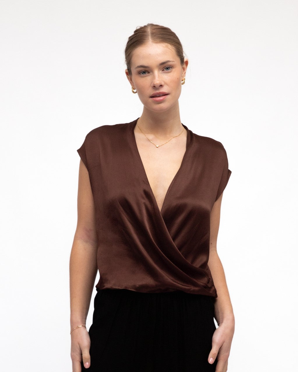Lady wearing White Closet's Hera Cross Over Satin Top in Chocolate Brown with a deep v-neck, short cap sleeves and a soft silky feel.