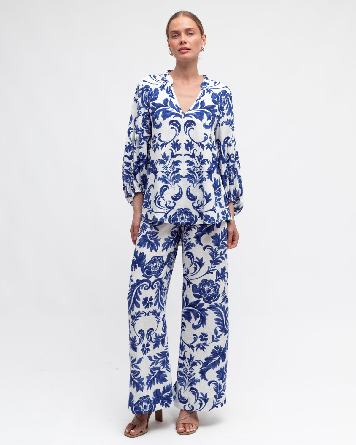 Woman wearing a blue and white floral top in baroque print by white closet.