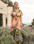 Model wearing the twist dress with strawberries and bulding print on a pink sunset background by white closet.